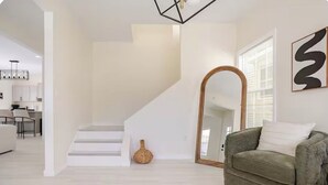 A modern living room with a staircase, a sofa, a mirror, and a vase.