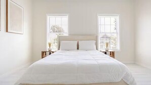 A bedroom with a large bed, two bedside tables, and a window with blinds.
