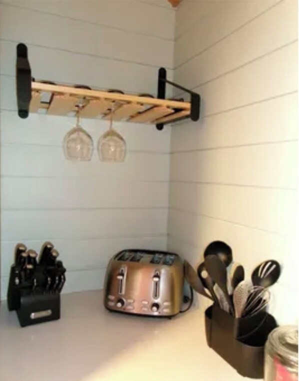 A kitchen with a toaster, wine glasses on a rack, and a utensil holder.