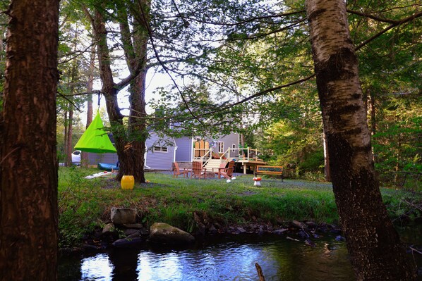 Un chalet au bord du lac, doté d’une terrasse et entouré d’arbres et d’un petit ruisseau.