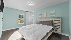 A bedroom with a bed, a TV, a window, and a door. - Villa Slate Coastal Country Retreat PCS • Nurses • Contractors- Weekly & Monthly (Jacksonville)