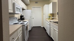 A narrow kitchen with white cabinets, a microwave, stove, and a refrigerator.