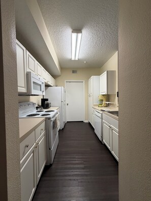 A narrow kitchen with white cabinets, a microwave, stove, and a refrigerator.