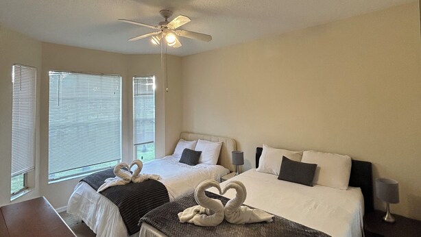 A hotel room with two beds, a ceiling fan, and large windows with blinds.