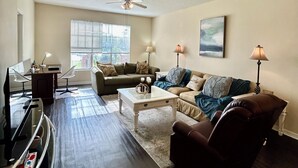 A living room with a dark wood floor, a white ceiling fan, a glass coffee table, two sofas, and a TV.