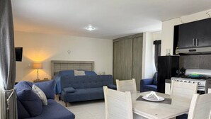 Un espacio habitable compacto con sofá, una mesa de comedor con sillas, kitchenette y cama.