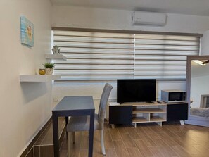 Um espaço compacto com área de jantar, TV de tela plana, micro-ondas e um pequeno sofá.