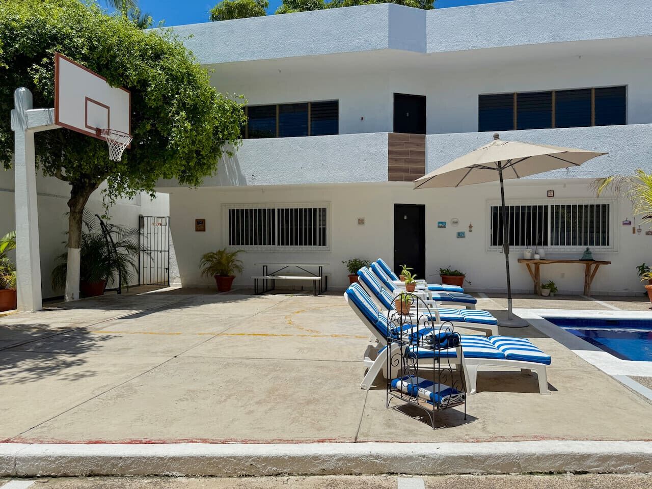 A poolside area with lounge chairs, a basketball hoop, and a pool.