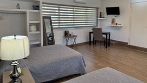Una habitación de hotel con cama, escritorio, silla, televisión y ventilador de techo.