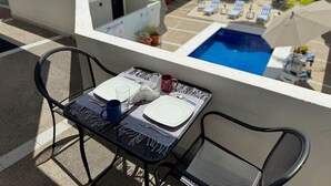A balcony with a table set for two, overlooking a swimming pool and lounge area.