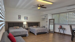 A hotel room with two beds, a ceiling fan, a desk, and a window with blinds.