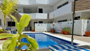 A pool area with a blue pool, white and blue striped lounge chairs, and potted plants.