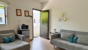 Una sala de estar con dos sofás grises, cada uno con una almohada azul con forma de mariposa, una mesita con una lámpara, un microondas y un refrigerador.