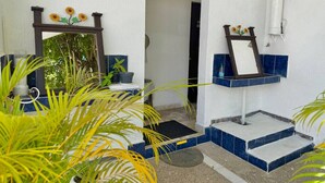 A bathroom with a white and blue tiled design, a mirror with a sunflower decoration, and a small sink area.