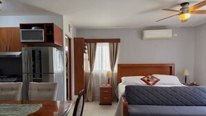 A hotel room with a bed, a desk with a chair, a microwave, a refrigerator, a ceiling fan, and an air conditioning unit.