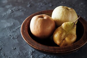 A wooden bowl containing three fruits on a textured surface.
