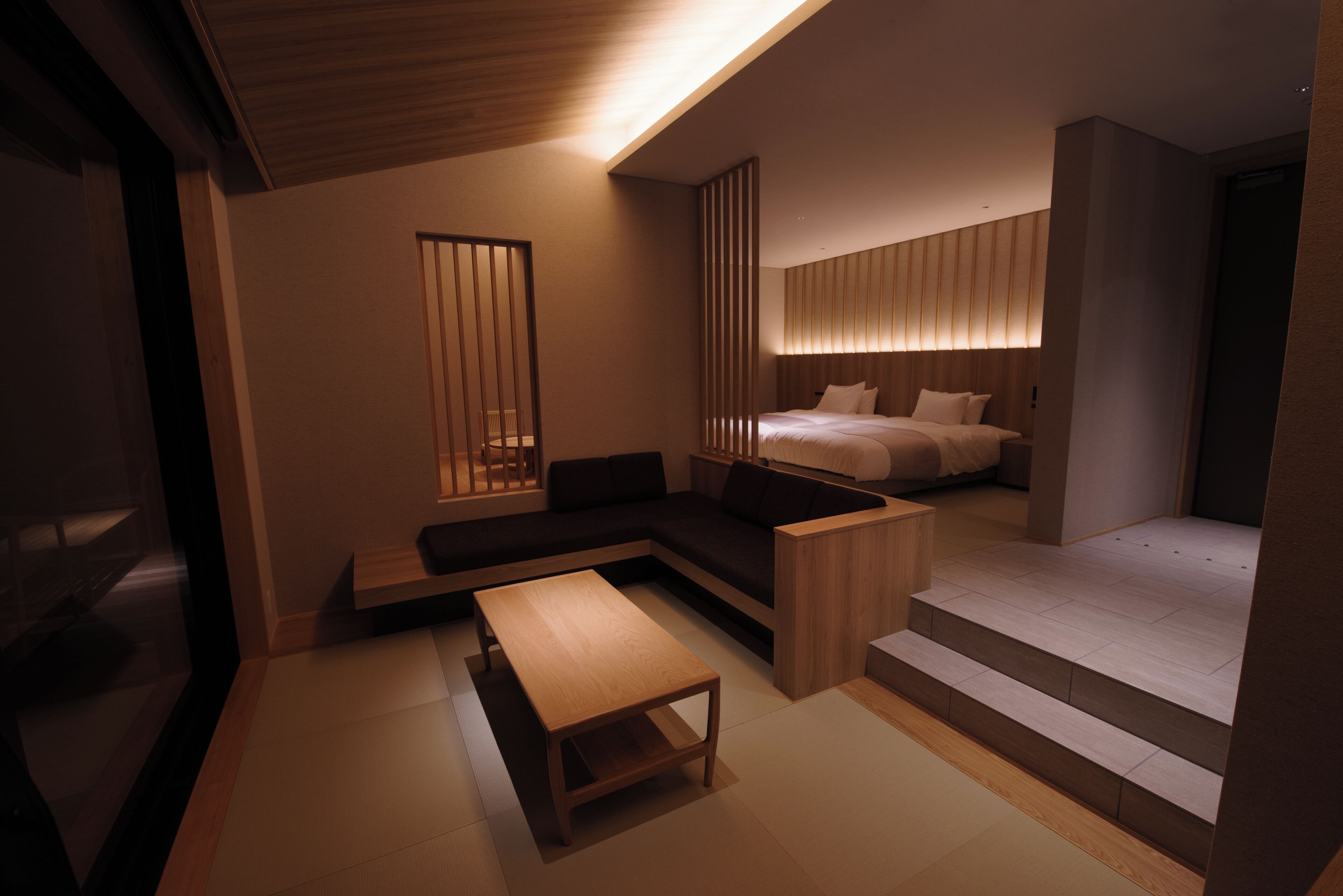 A modern hotel room with a sofa, a wooden table, and a bed with a headboard.