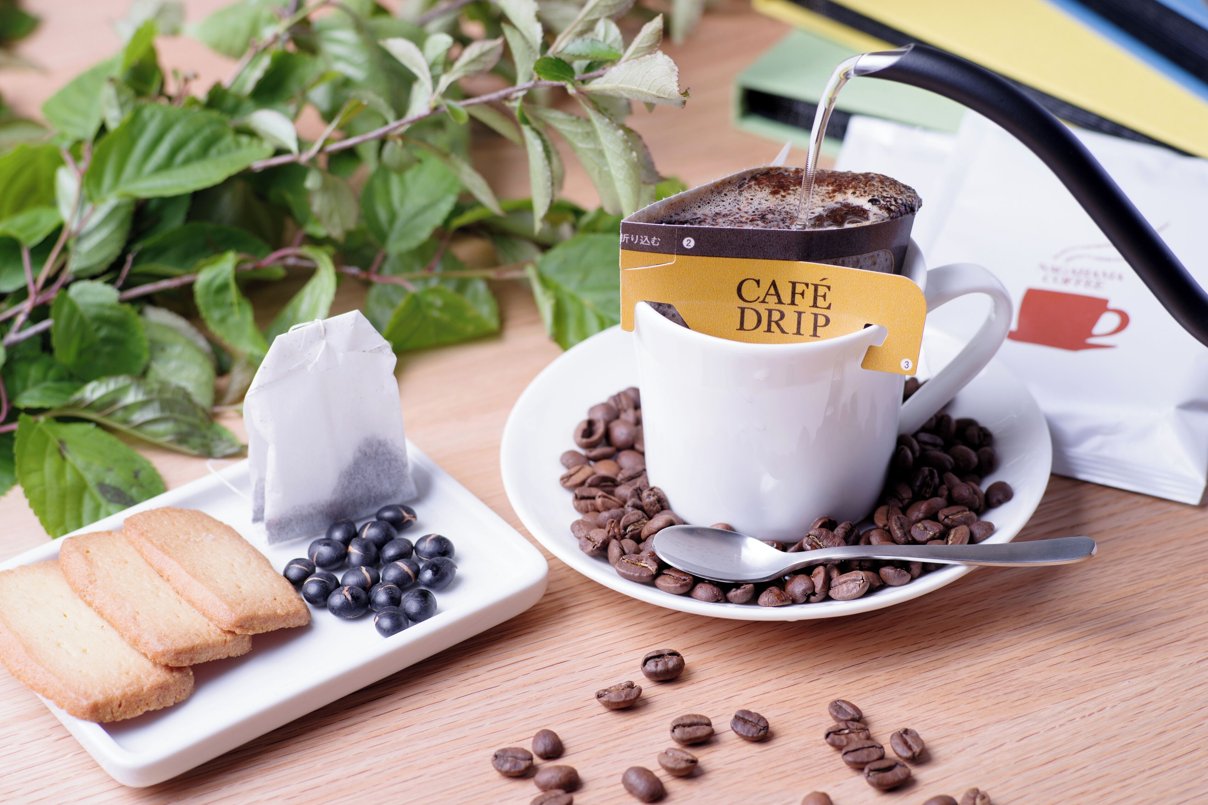 A white cup with a coffee drink, a tea bag, and a spoon on a saucer.