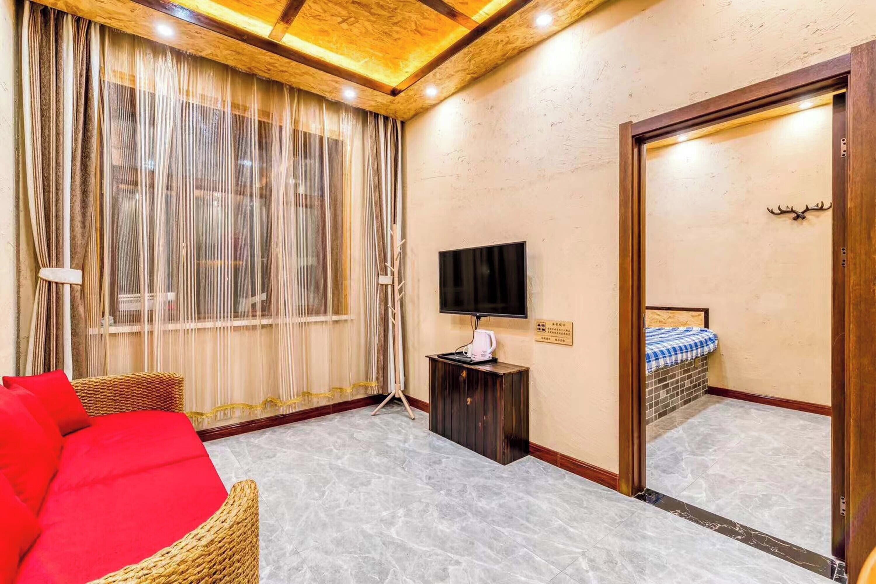 A hotel room with a large window, a television, a red sofa, and a wooden door.