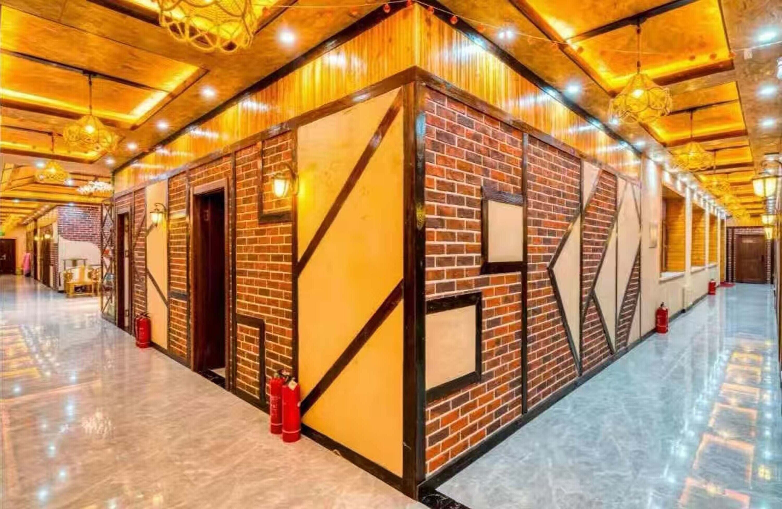 A spacious corridor with a brick wall and wooden beams, fire extinguishers, and hanging lights.