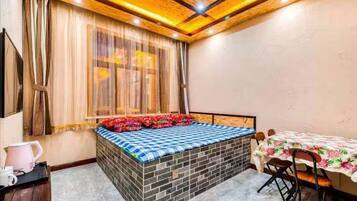 Un dormitorio con cama, una mesa, sillas, un ventanal con cortinas e iluminación empotrada en el techo.