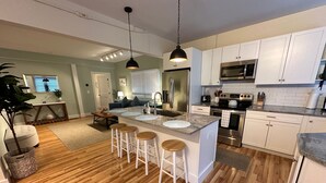 A modern kitchen with white cabinets, stainless steel appliances, and a central island with bar stools. - 86 Dr Marcus House - Popular Broadway Area (Newport)