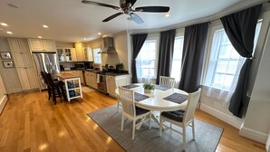 A modern kitchen with white cabinets, a stainless steel refrigerator, and a dining area with a round table and chairs. - 86 Dr Marcus House - Popular Broadway Area (Newport)