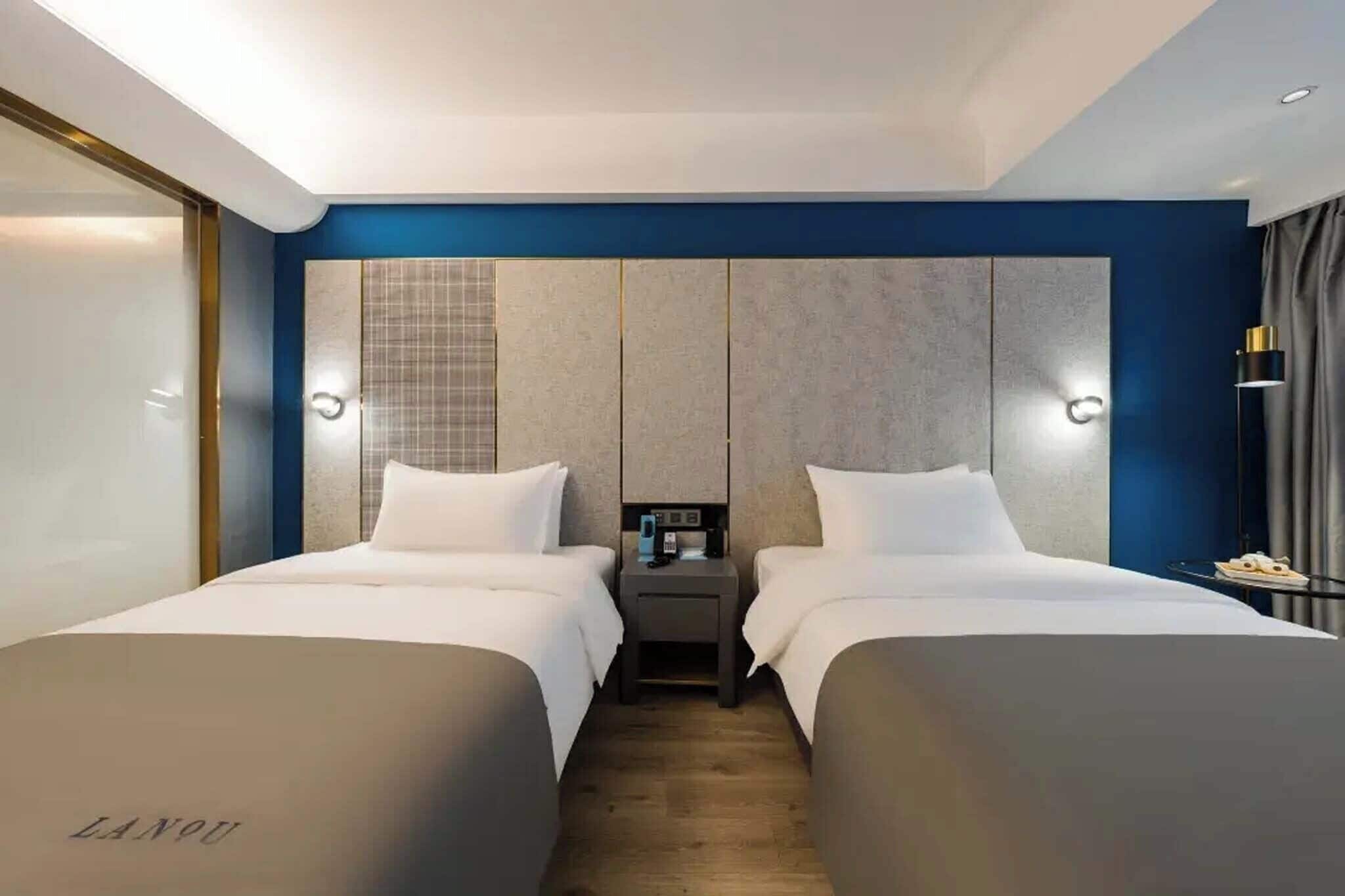 A hotel room with two beds, a nightstand with a lamp, and a large wall panel.