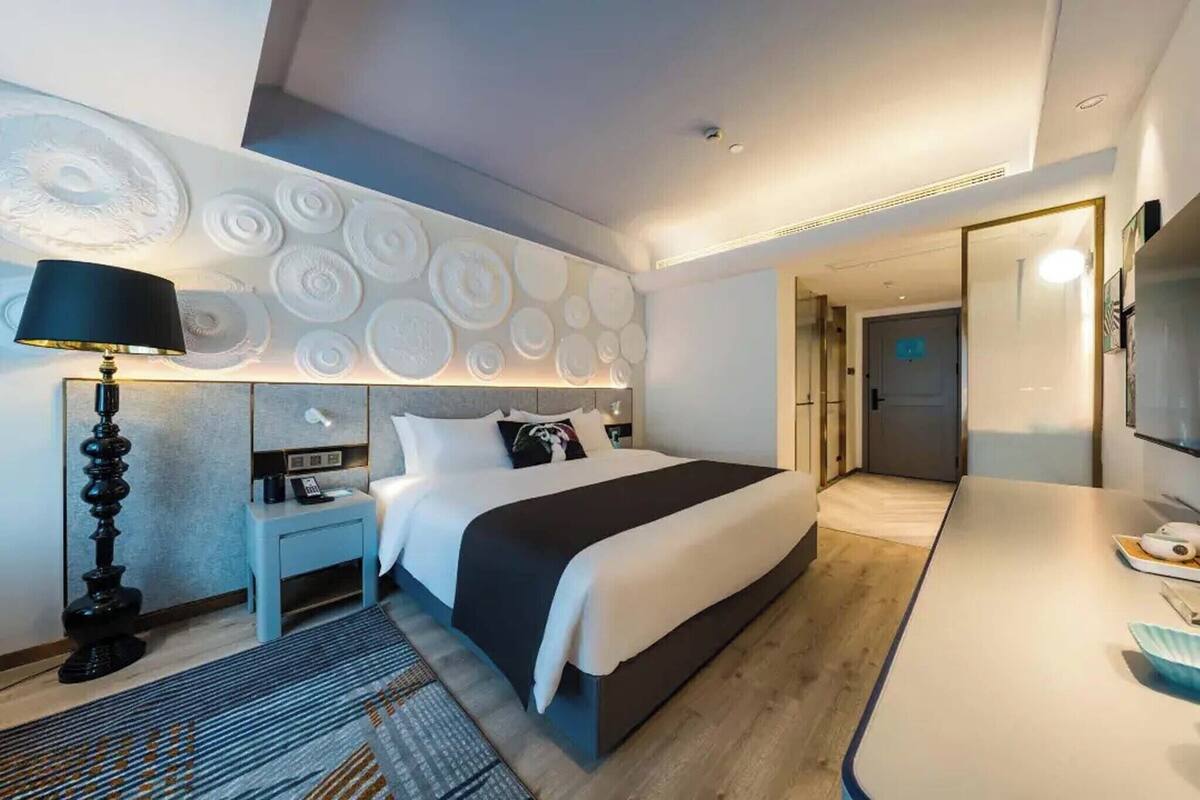 A modern hotel room with a large bed, bedside tables, a desk, and a TV.