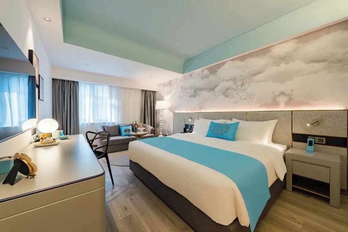A modern hotel room with a large bed, a desk, and a seating area.