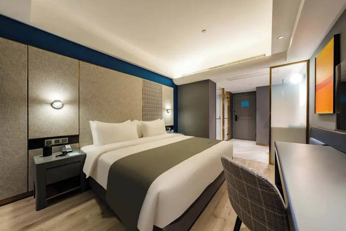 A modern hotel room with a large bed, bedside tables, a desk, and a chair.