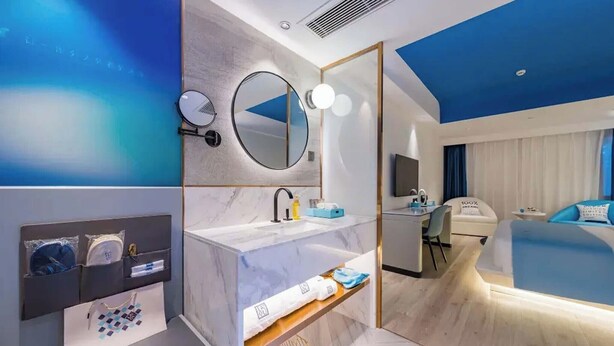 A modern hotel room with a marble vanity, a round mirror, a desk with a chair, and a bed with blue bedding. - Shanghai Lujiazui BaBaiBan LANOU Hotel (Shanghai)
