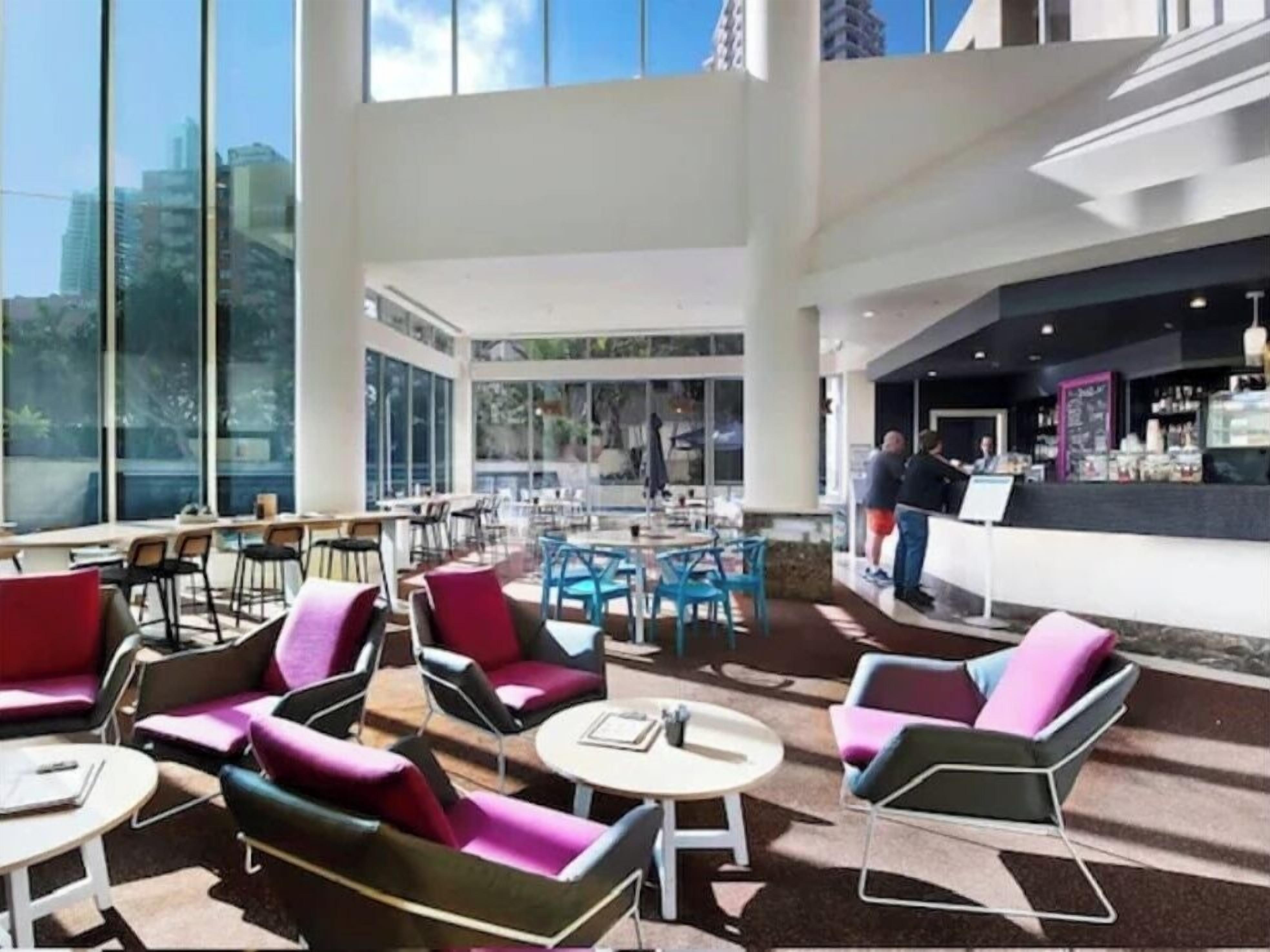 A spacious indoor area with multiple seating arrangements, a bar area, and large windows providing views of the cityscape.