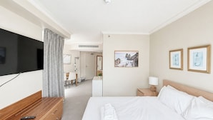 A hotel room with a bed, a TV, a desk, and a bathroom visible through an open door. - Queen Studio | Beach and Tram at Doorstep @ Legend (Surfers Paradise)