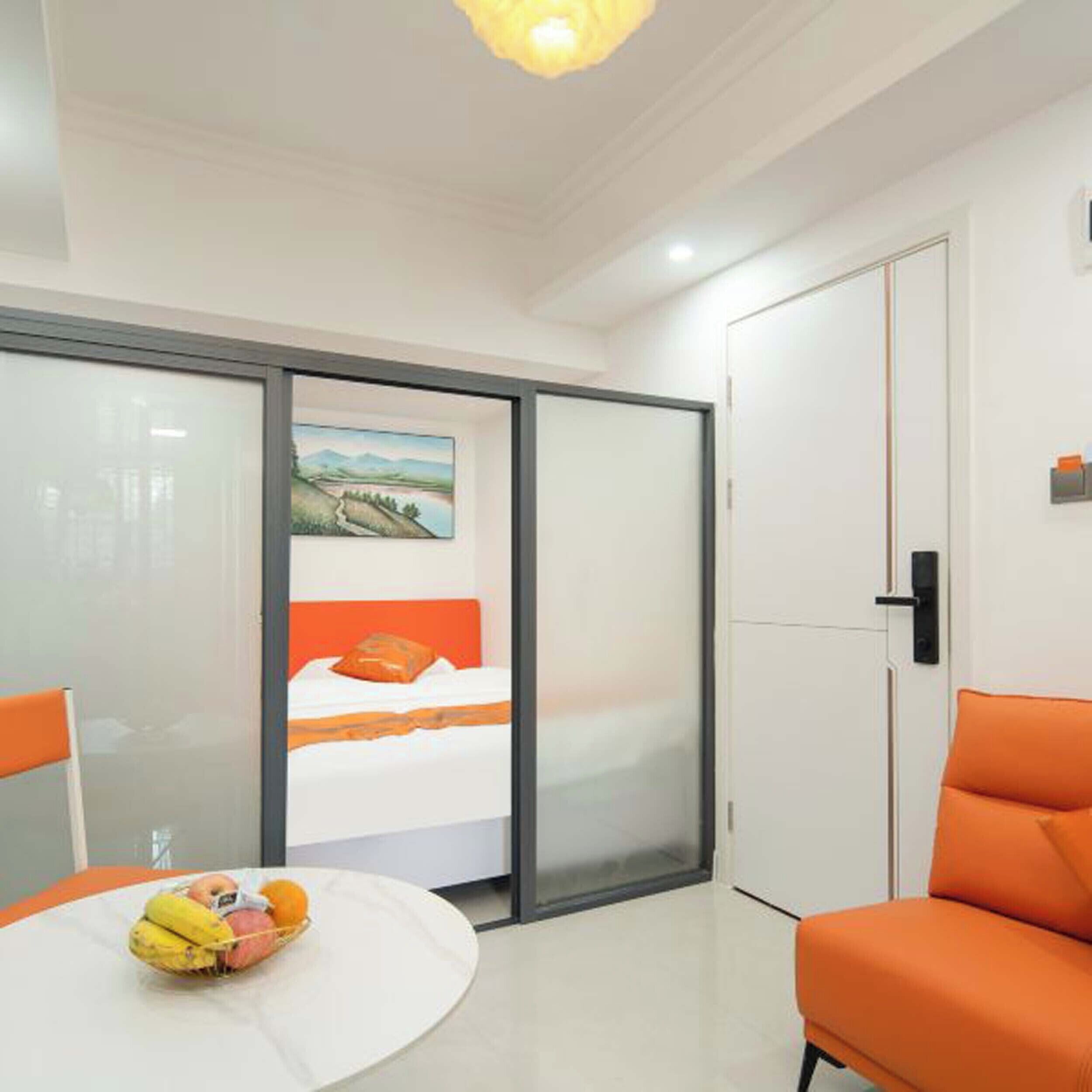 A modern hotel room with a bed, a dining table with fruit, and a bright orange chair.