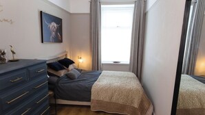A bedroom with a bed, dresser, and a window with curtains. - Cosy 1-Bedroom Flat, Walk to Beaches (South Ayrshire)