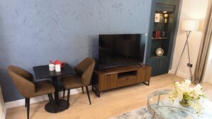 A modern living room with a flat-screen TV, two brown chairs, a small table with a coffee pot, a glass coffee table with flowers, and a lamp. - Cosy 1-Bedroom Flat, Walk to Beaches (South Ayrshire)