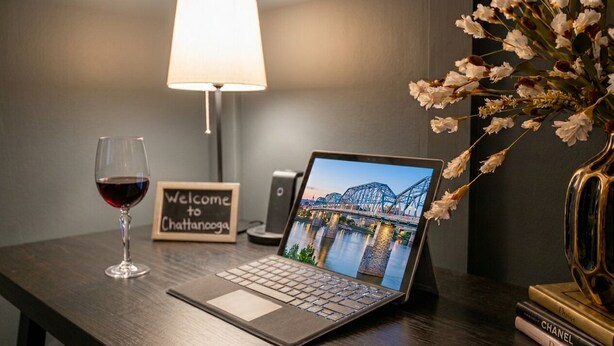 A laptop on a desk with a 'Welcome to Chattanooga' sign, a glass of red wine, a lamp, and a vase with flowers. -     Spotless Luxury Retreat. Walk to Food & Fun. King Bed. Free Parking (Chattanooga)