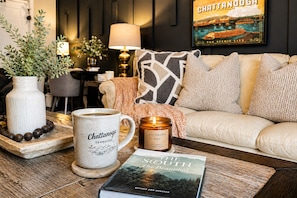 A cozy living room with a white sofa, a coffee mug, a candle, and a book on a wooden coffee table.