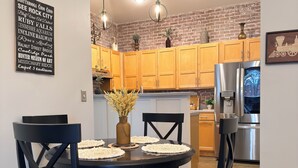 A dining area with a round table, black chairs, and a patterned rug. There is a brick wall and wooden cabinets in the background. -     Spotless Luxury Retreat. Walk to Food & Fun. King Bed. Free Parking (Chattanooga)