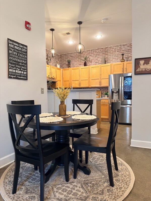 A dining area with a round table, black chairs, and a patterned rug. There is a brick wall and wooden cabinets in the background. -     Spotless Luxury Retreat. Walk to Food & Fun. King Bed. Free Parking (Chattanooga)