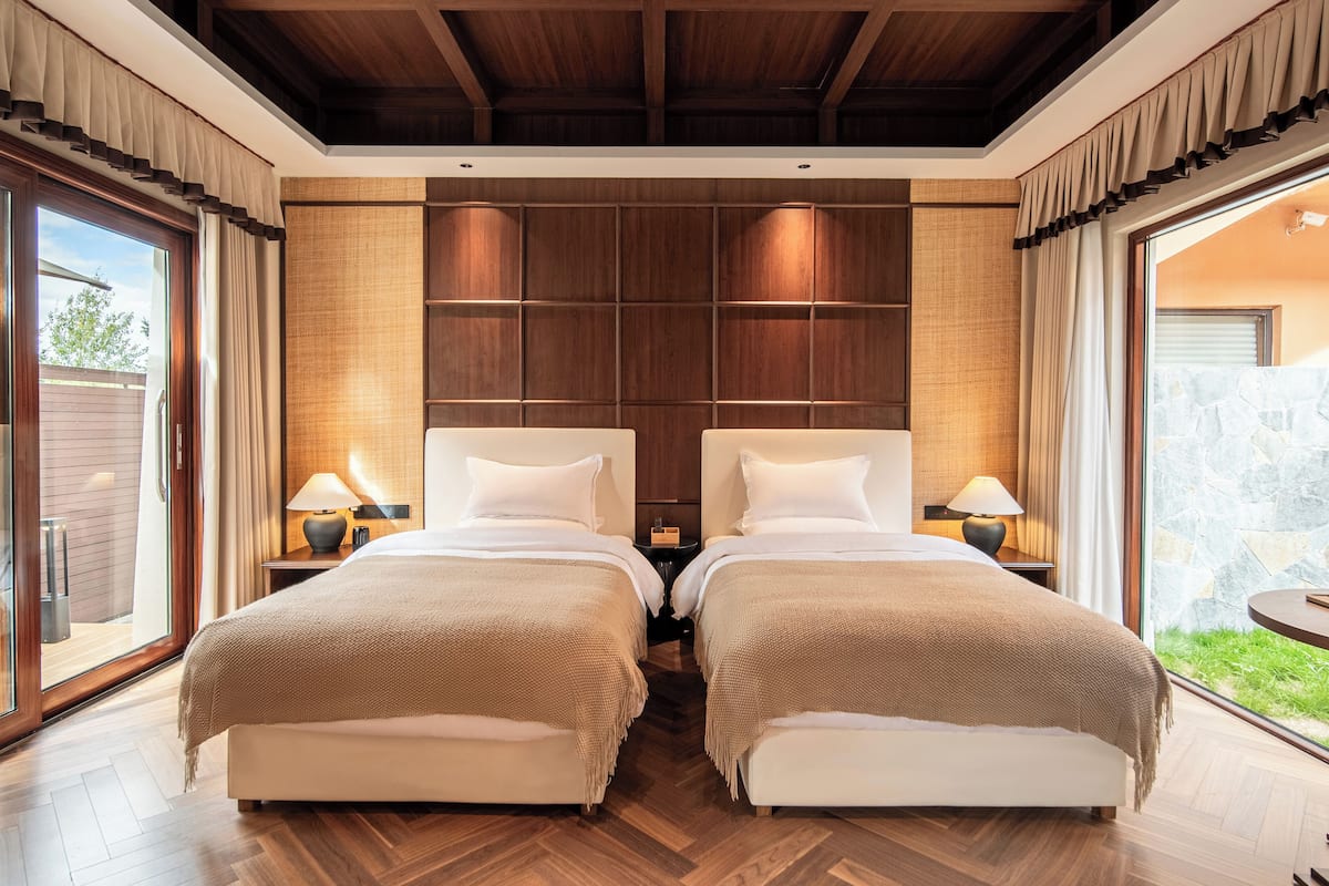 A double room with two beds, wooden paneling, and a view of greenery.