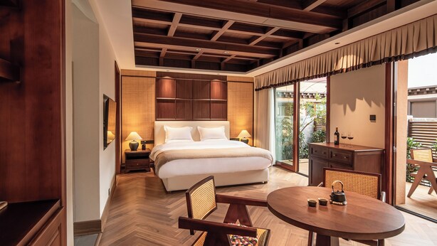 A bedroom with a large bed, bedside tables, a wooden ceiling, and a view of the outdoors.
