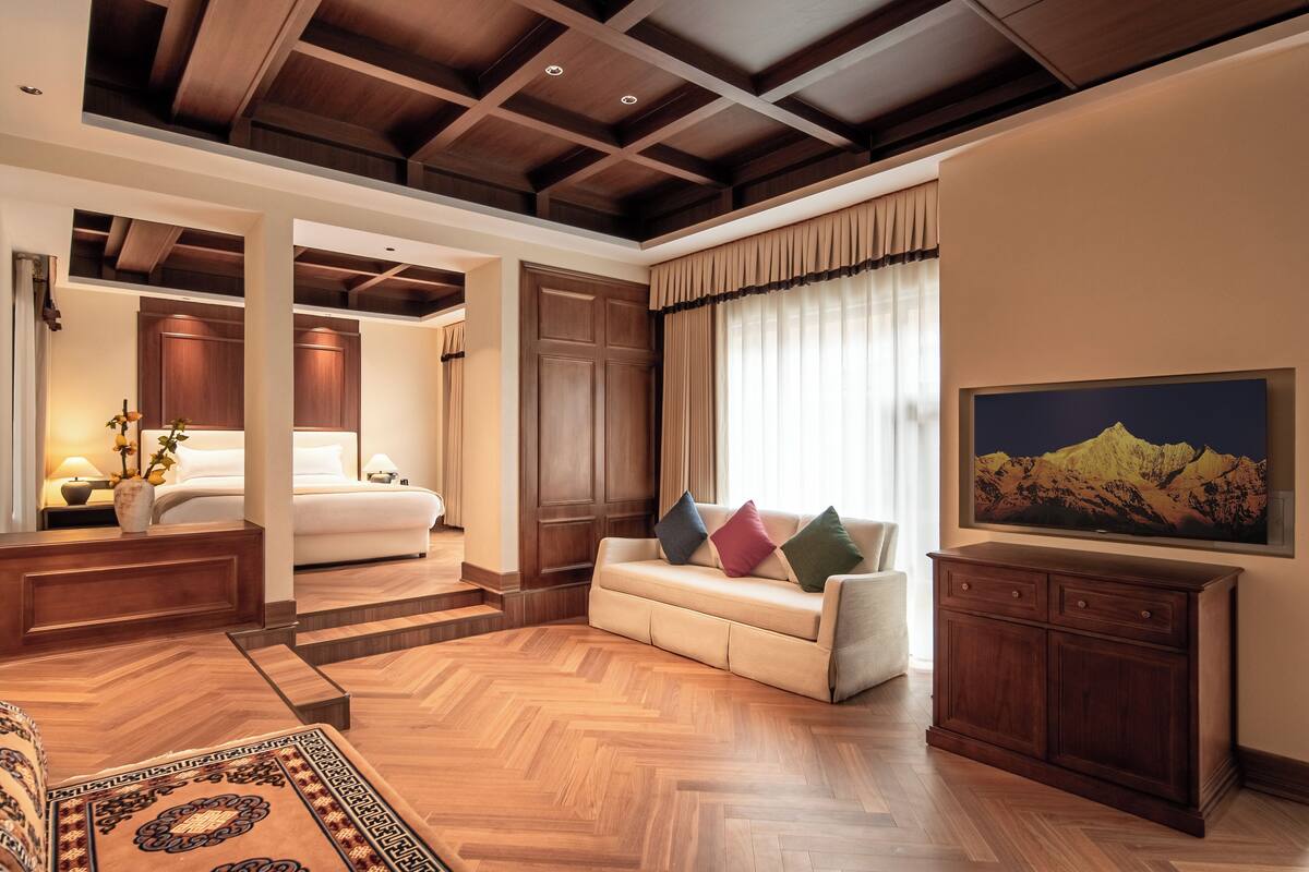A spacious room with a wooden floor, a sofa with colorful cushions, a large painting, and a wooden cabinet.