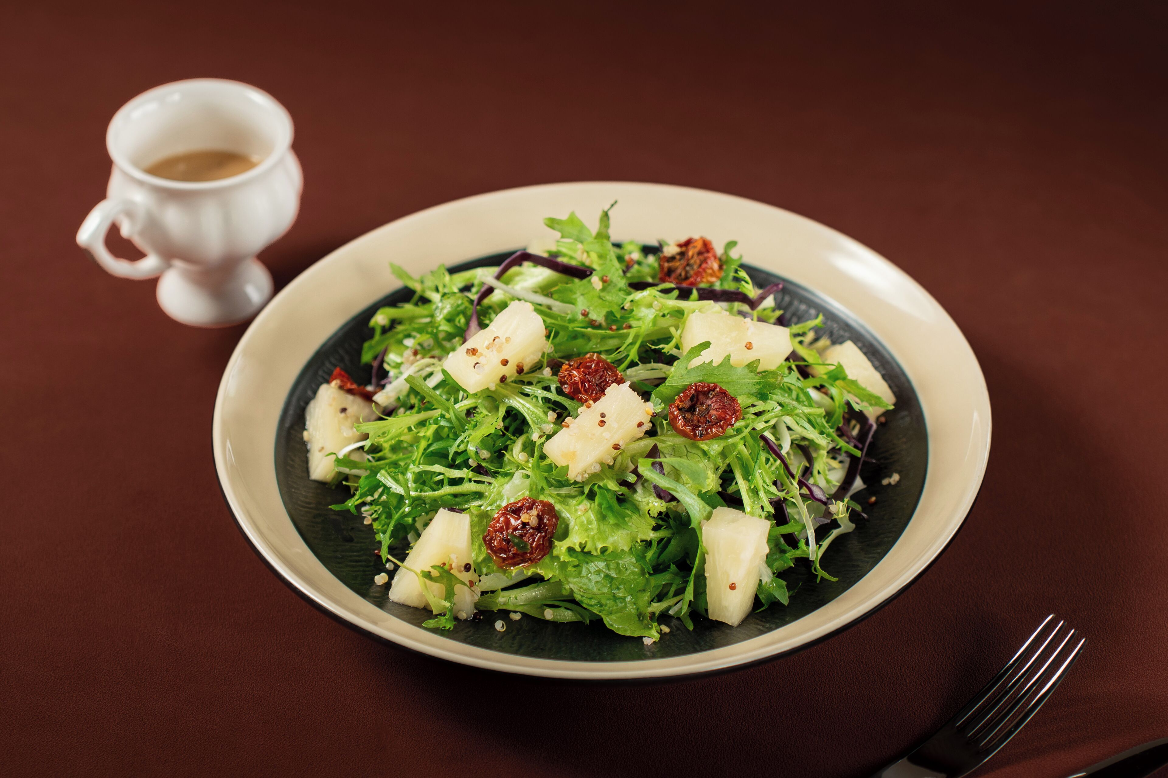 A plate of salad with croutons and dried cranberries on a dark table.