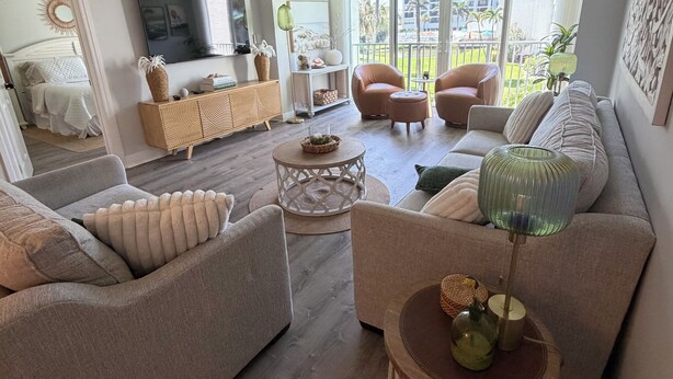 A modern living room with a sofa, armchairs, a TV, and a balcony with a view.
