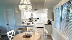 A dining area with a round wooden table, white chairs, and a chandelier.