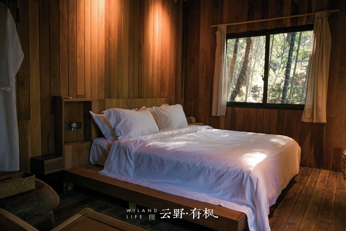 A wooden cabin bedroom with a bed, a window with curtains, and a small wooden bench.