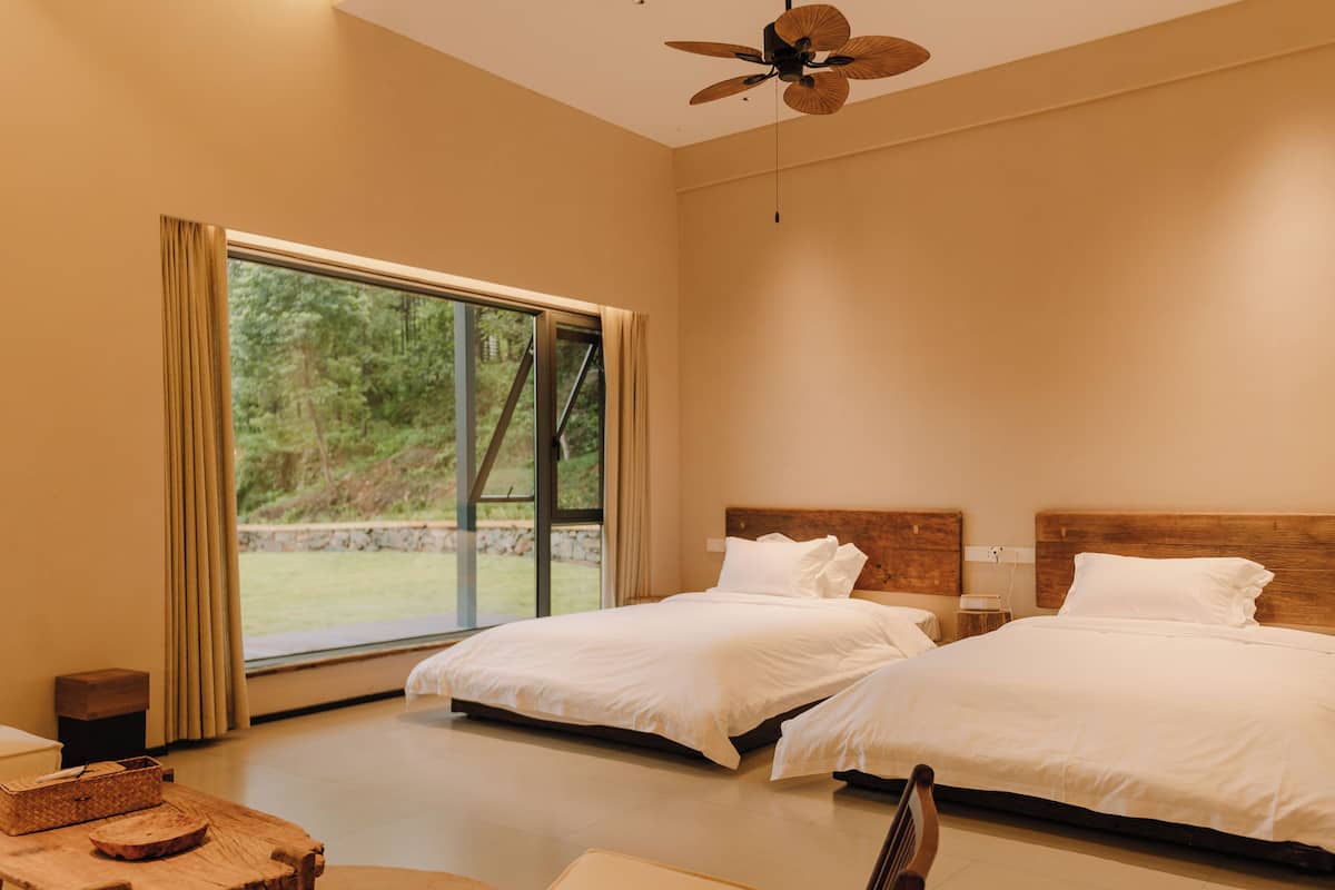 A modern bedroom with two beds, a ceiling fan, and a large window with curtains.