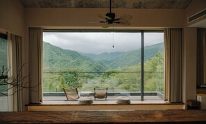 A room with a large window offering a view of lush green mountains. There are two wicker chairs and a small round table on the windowsill. - Yunye Youfengwei Vacation Homestay (Changsha)